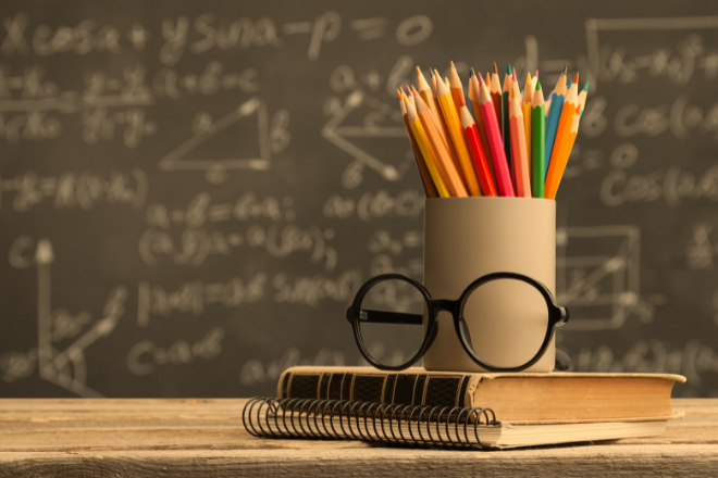 Chalkboard with equations, desk with pencils and spectacles in a classroom for Blog What do i need to qualify for an Australian visa as a teacher